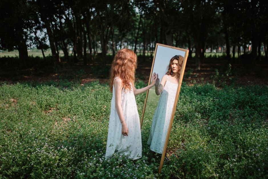 Woman reaching toward her reflection in a mirror outdoors